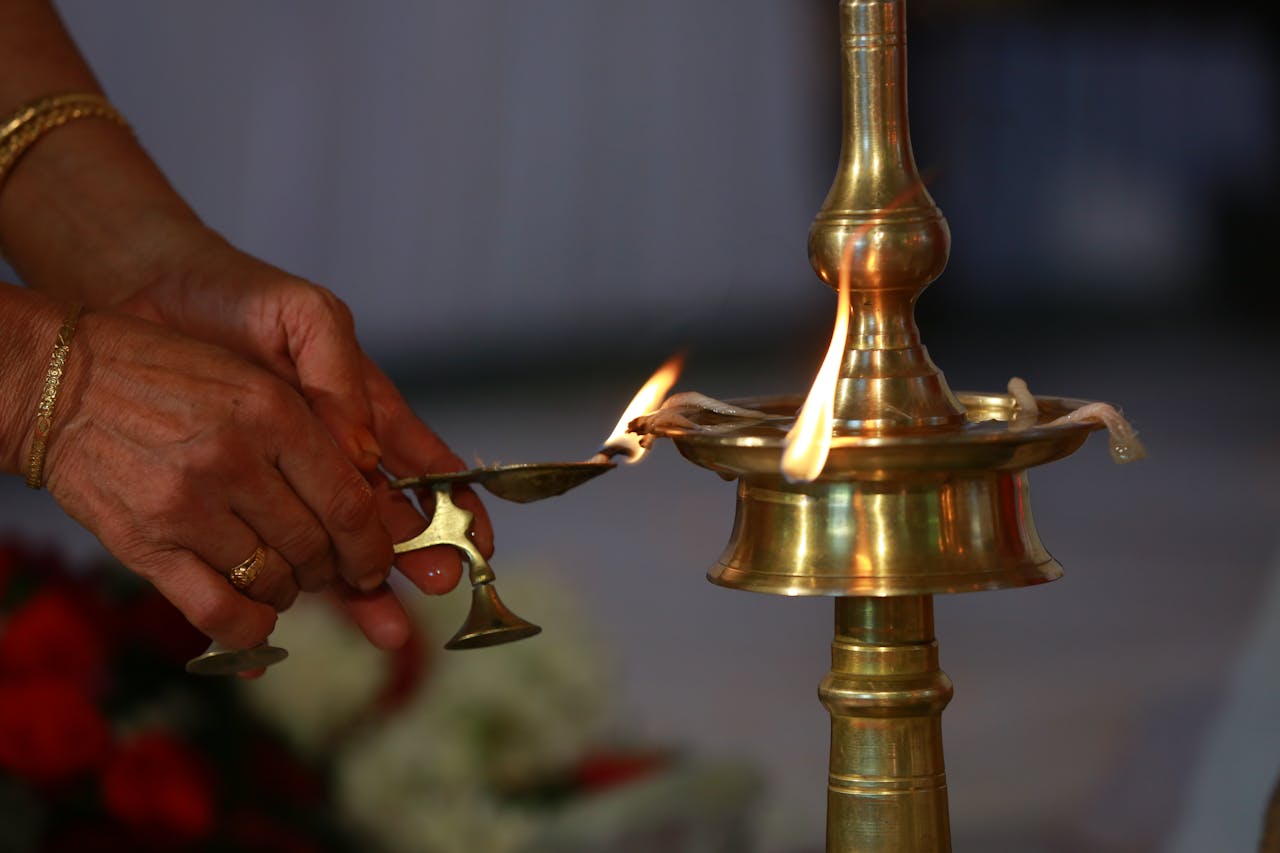 Close-up of hands lighting an oil lamp during a traditional Indian ceremony, symbolizing spirituality and tradition.